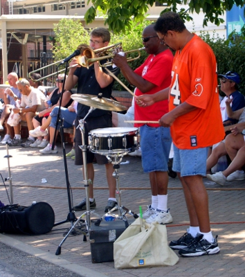 [Trumpet player with a trumbone player to his right and a drummer to his left.]